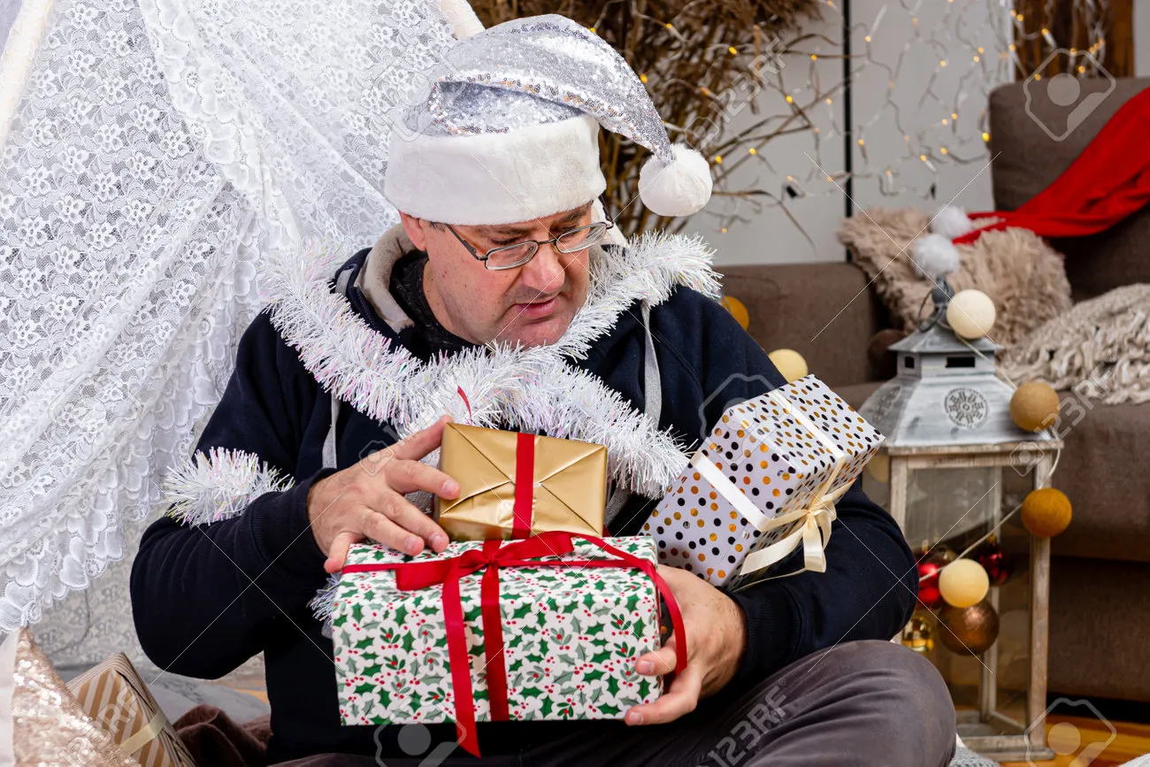 171800143-middle-aged-man-with-glasses-and-a-silver-dwarf-hat-with-christmas-gift-boxes-in-a-decorated-room